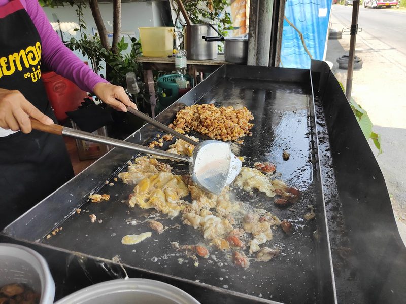 ผัดแป้งหอยทอดและสับให้แตกเป็นชิ้นบนกระทะแบนใบใหญ่