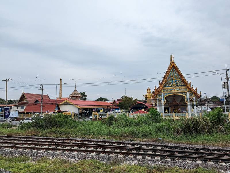 หน้าบันโบสถ์ลายทองของวัดธรรมนิยม หลังรางรถไฟและพงหญ้า